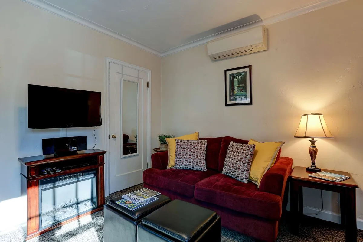A stylish interior with a vibrant red couch facing a modern flat-screen TV, paired with a table lamp and a chic coffee table. The room is arranged for comfort and entertainment, making it ideal for movie nights or cozying up after a day exploring town.