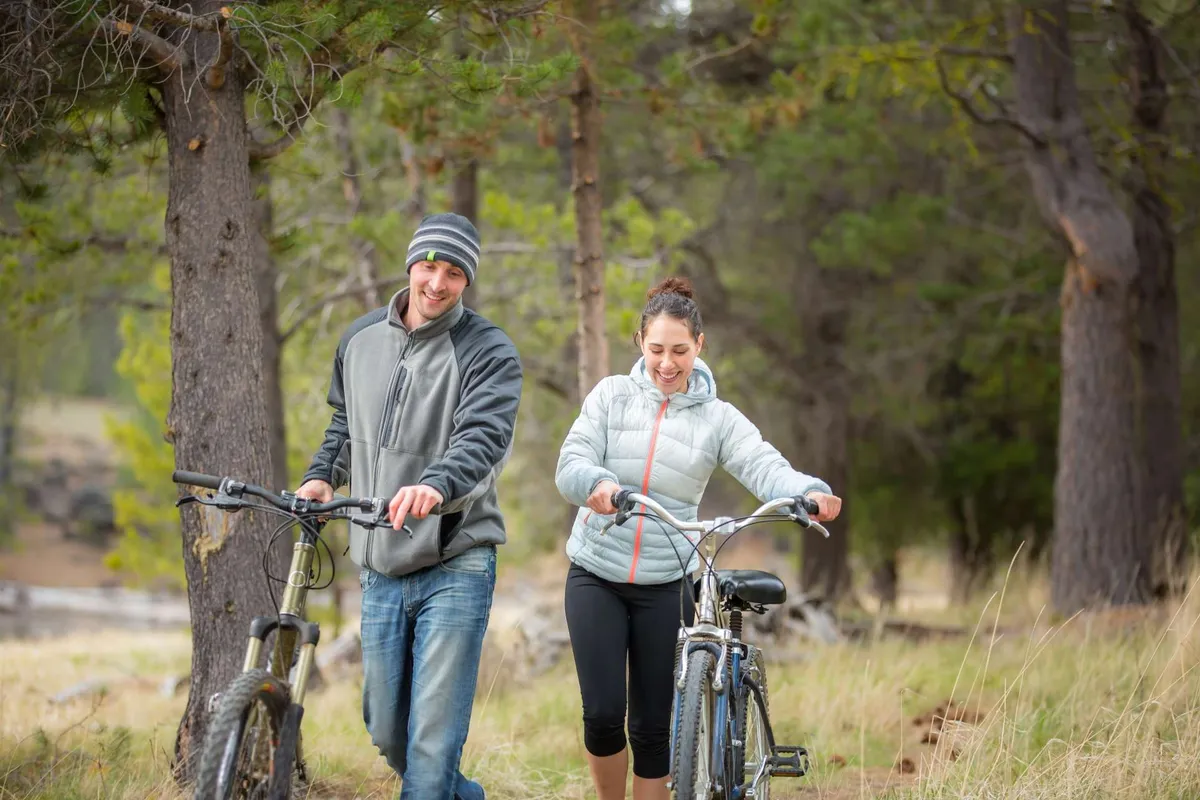 A playful exterior shot showing a couple walking alongside parked bicycles, with trees providing a lush canopy. The mood is lively and social, suggesting the ease of exploring the neighborhood by foot or bike, and the joy of discovering local hotspots nearby.