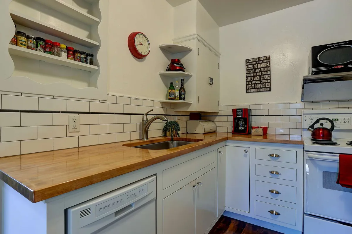 This image features a cozy kitchenette with a wooden countertop, classic white cabinetry, modern kitchen appliances (including a visible stove and spice rack), and warm, inviting lighting. The countertop offers ample space for meal preparation, while the cabinetry and shelving showcase a harmonious blend of vintage-inspired and contemporary design elements.