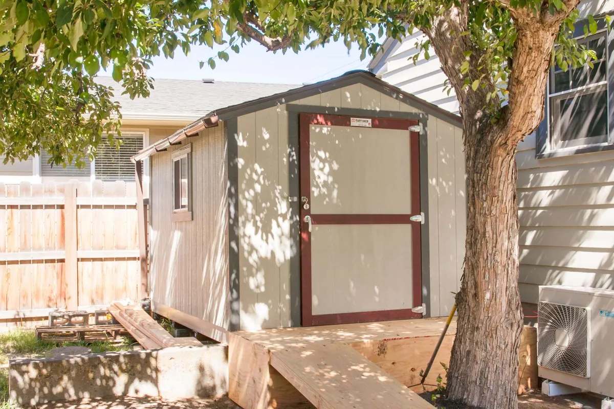 An inviting exterior scene featuring a well-kept patio area adjacent to a charming shed, with a tree and pathway leading into the yard. The setting hints at a tranquil outdoor space perfect for relaxing after a day exploring the city, and brings the transition from indoor to outdoor living to life.