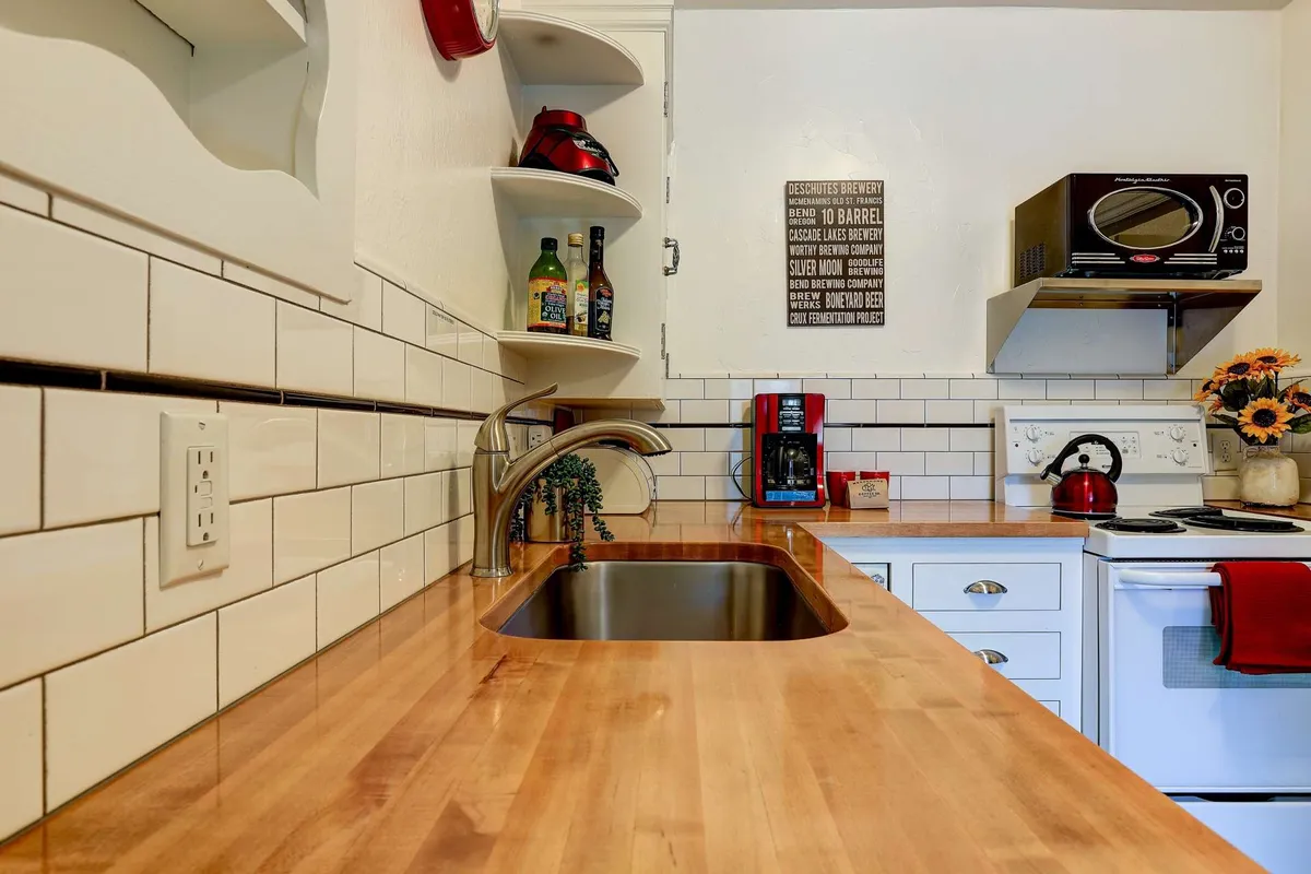 A closer look at the kitchen sink area, featuring a wooden countertop, open shelving with bottles, a coffee maker, and decorative flowers. The space is arranged for both practicality and cozy morning rituals, highlighting the coffee-making amenity.